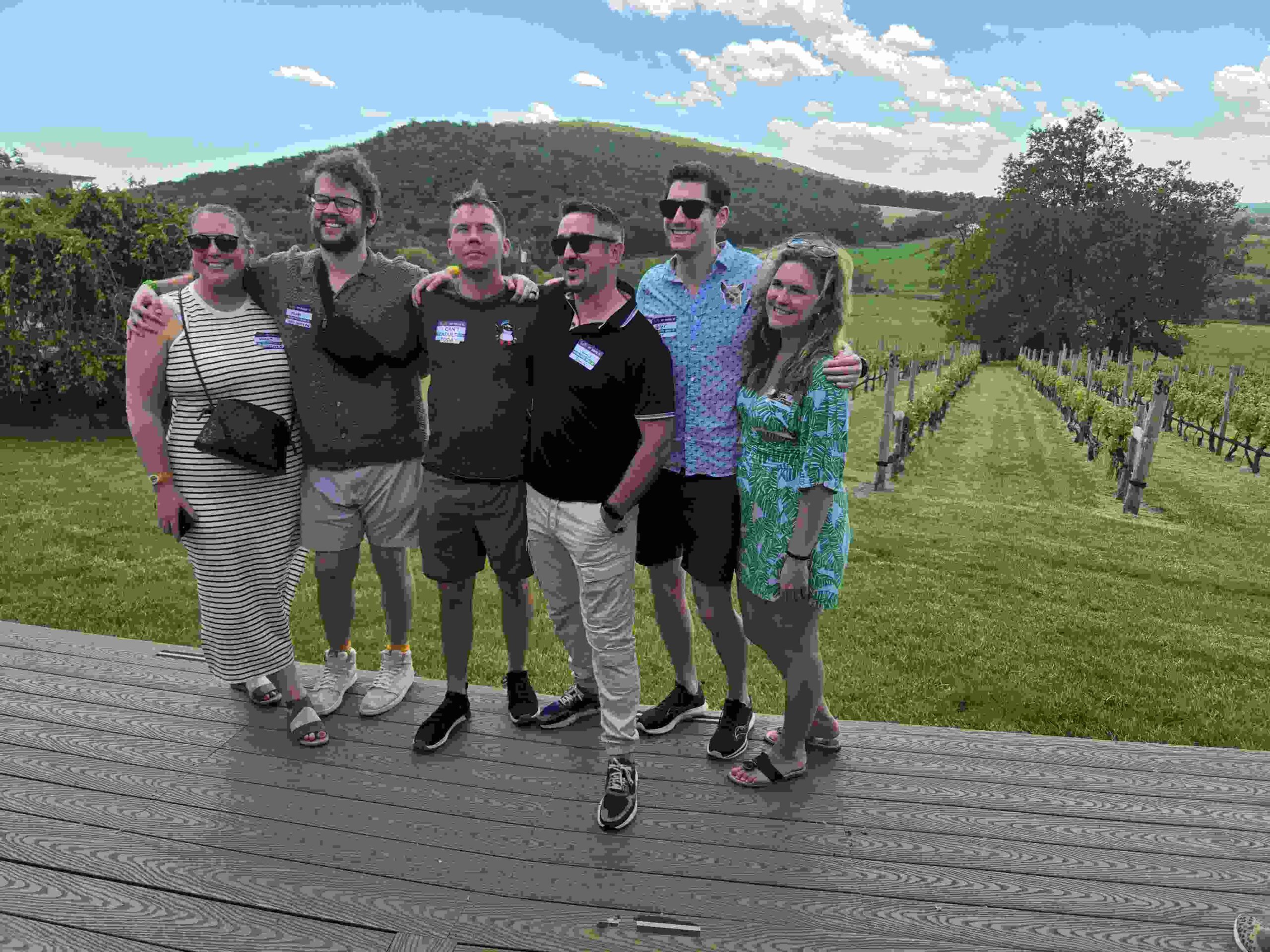 A group of friends posing together with vineyard and mountain views