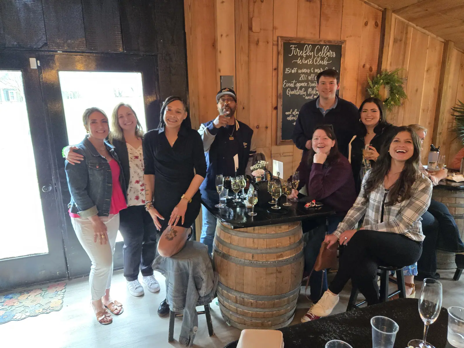 A tour group gathered around wine bottles in a winery barrel room