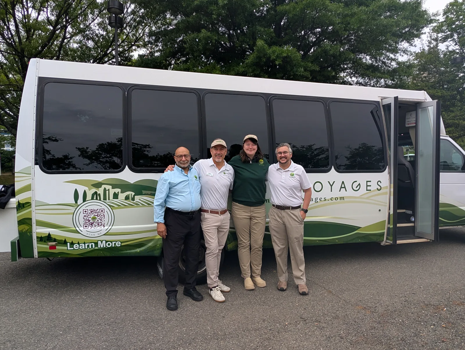 Four members of the Vineyard Voyages team standing in front of the branded executive coach